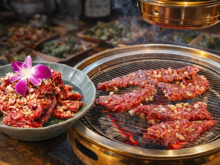 한우 마늘양념 숯불구이. 양념한 한우가 숯불 화로 위 석쇠에서 구워지고 있다.