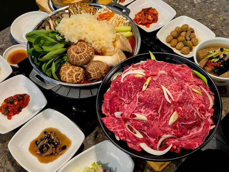 한우얼큰전골 한상. 같은 재료에 얼큰한 육수를 쓴 전골이 밑반찬과 함께 차려져 있다.