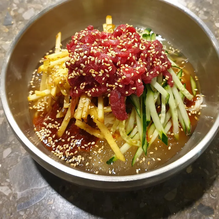 한우육회비빔국수. 국수 위에 한우 육회와 채 썬 채소가 올려져 있다.